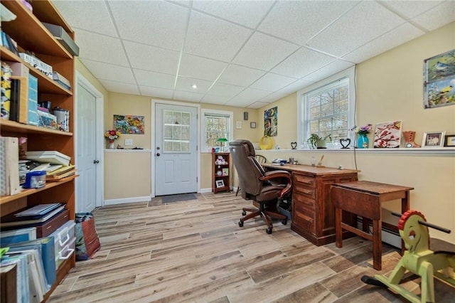 office area featuring light wood-type flooring, a baseboard heating unit, baseboards, and a drop ceiling