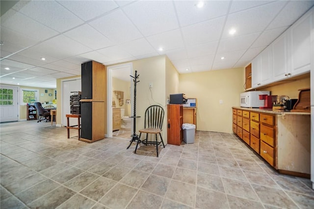 kitchen with a drop ceiling, light tile patterned floors, white microwave, and white cabinetry