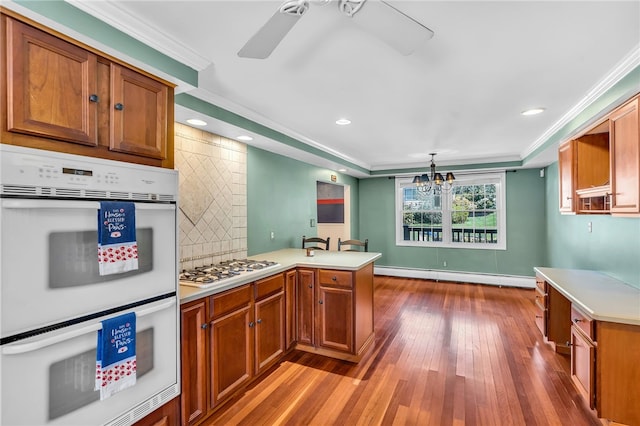 105 Quaker Dr, West Warwick, RI 02893 - kitchen with a peninsula, brown cabinetry, dark wood-type flooring, white appliances, and a baseboard radiator