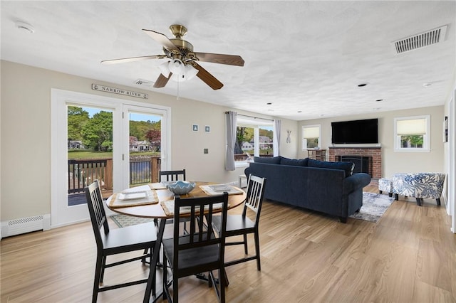106 N River Dr, Narragansett, RI 02882 - dining space featuring a baseboard heating unit, a ceiling fan, light wood finished floors, and a brick fireplace