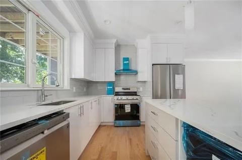 70 Shady Ln, Burrillville, RI 02859 - kitchen with appliances with stainless steel finishes, a sink, wall chimney exhaust hood, white cabinetry, and light wood-type flooring