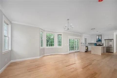 70 Shady Ln, Burrillville, RI 02859 - unfurnished living room with a chandelier, baseboards, light wood-style floors, and ornamental molding