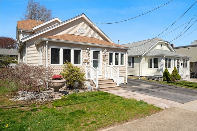 view of front of house featuring roof with shingles, entry steps, and a front yard