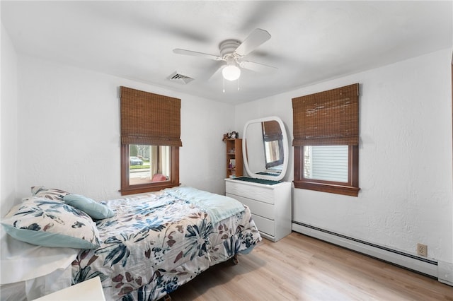 bedroom featuring visible vents, light wood-style flooring, ceiling fan, and a baseboard heating unit
