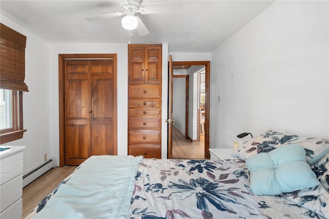 bedroom featuring a closet, ceiling fan, a baseboard heating unit, and light wood-type flooring