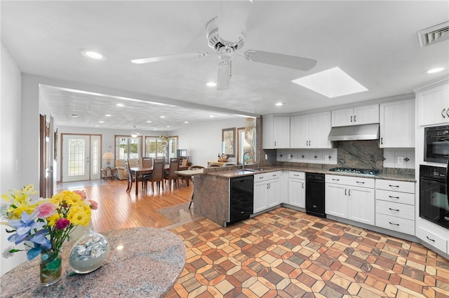 kitchen featuring a peninsula, under cabinet range hood, a sink, black appliances, and a skylight