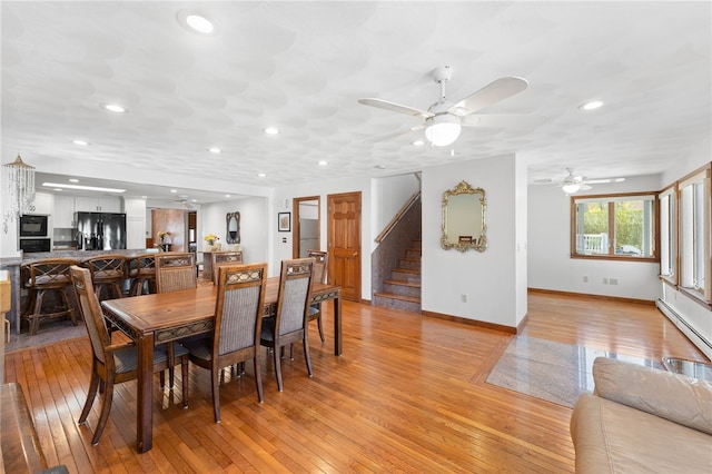 dining area with light wood-style floors, a ceiling fan, baseboards, a baseboard heating unit, and stairway