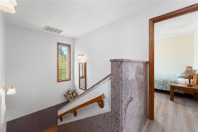 hallway featuring visible vents, wood finished floors, and an upstairs landing