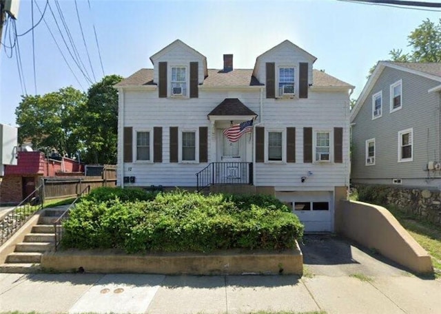 cape cod house with an attached garage, driveway, and a chimney