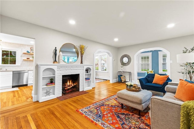 living room featuring light wood-style floors, a fireplace, arched walkways, and recessed lighting