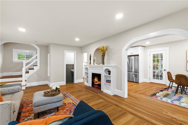living area featuring arched walkways, recessed lighting, baseboards, and light wood-type flooring