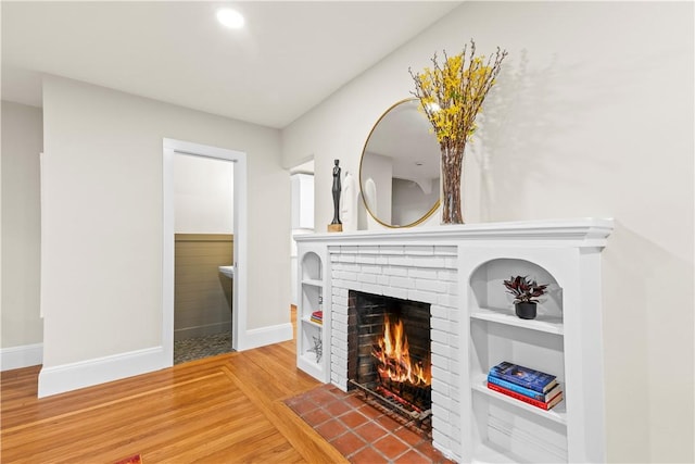 unfurnished living room featuring wood finished floors, baseboards, and a brick fireplace