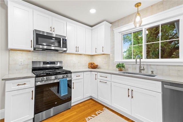kitchen with light wood finished floors, a sink, stainless steel appliances, white cabinetry, and tasteful backsplash
