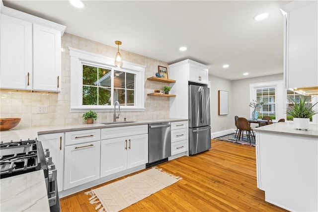 kitchen with a sink, white cabinetry, stainless steel appliances, tasteful backsplash, and light wood-type flooring