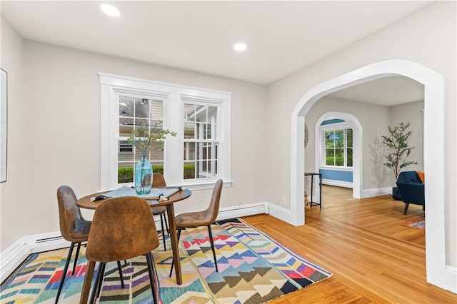 dining space with a baseboard heating unit, recessed lighting, arched walkways, baseboards, and light wood-style floors