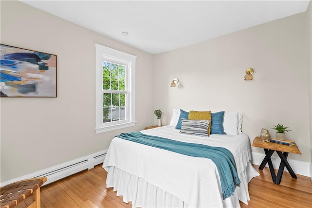bedroom featuring a baseboard heating unit, light wood-style floors, and baseboards