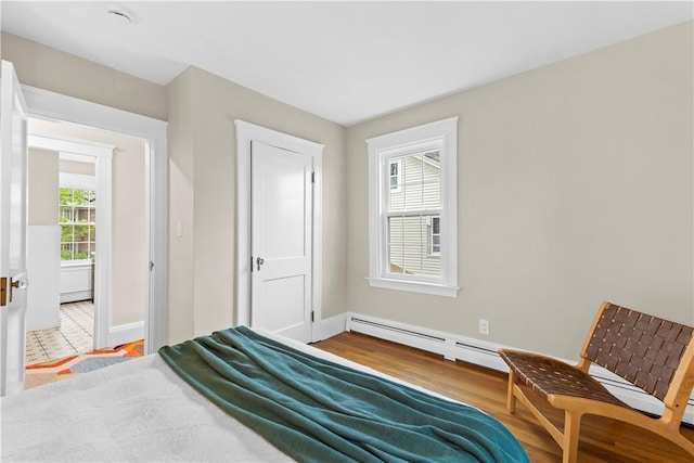 bedroom with a baseboard radiator, multiple windows, light wood-style flooring, and baseboards