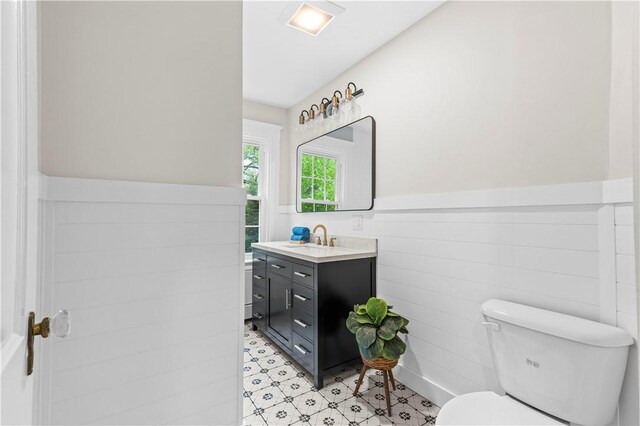 bathroom featuring toilet, tile patterned floors, vanity, and a wainscoted wall