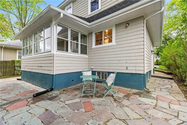 view of property exterior featuring a patio, a sunroom, a shingled roof, and fence