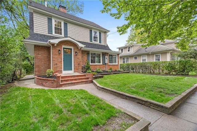 view of front of house with roof with shingles, a chimney, brick siding, and a front yard