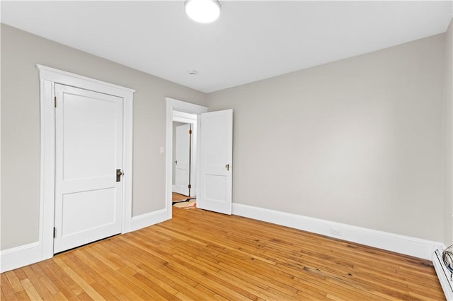 unfurnished bedroom featuring a baseboard heating unit, baseboards, and light wood-style floors