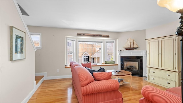 living room featuring a tiled fireplace, light wood-style flooring, and baseboards
