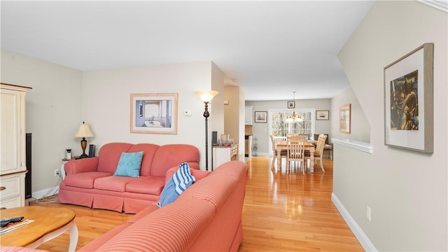 living room with a chandelier, baseboards, and light wood-type flooring