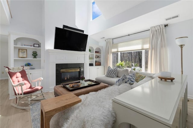 living area with visible vents, a wealth of natural light, light wood-style flooring, and a towering ceiling