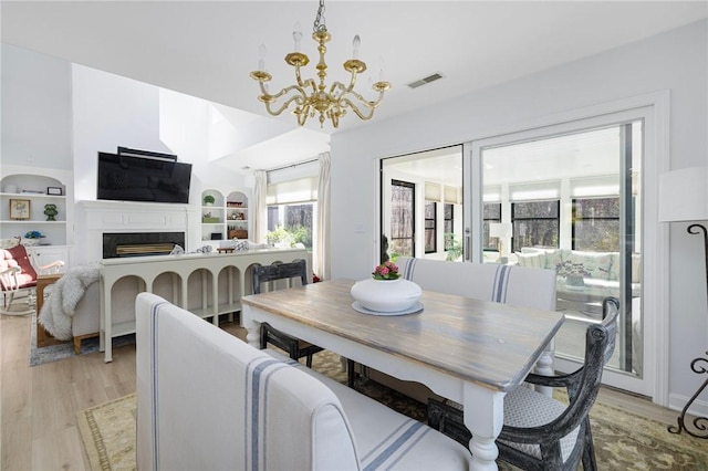 dining space with visible vents, built in features, a fireplace, light wood-type flooring, and a notable chandelier