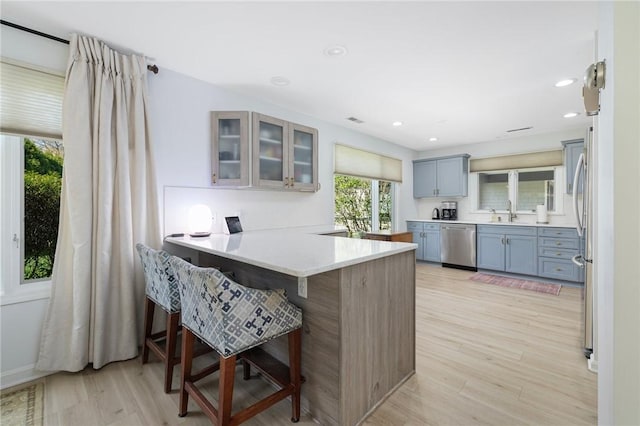 kitchen featuring a peninsula, a breakfast bar, glass insert cabinets, light wood finished floors, and appliances with stainless steel finishes