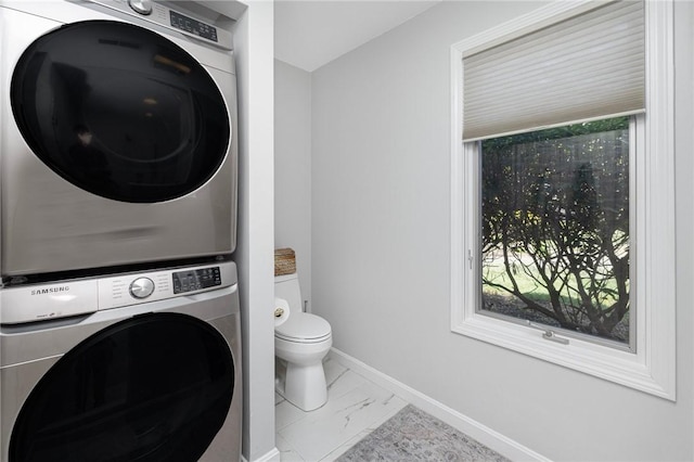 bathroom featuring baseboards, stacked washer and clothes dryer, marble finish floor, and toilet