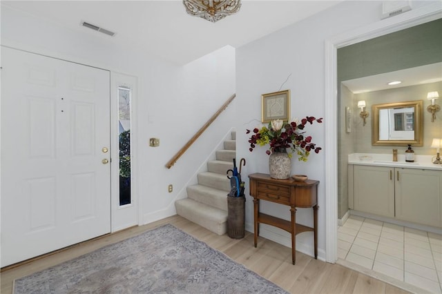 entryway with visible vents, light wood-style flooring, baseboards, and stairway