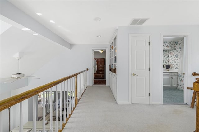 corridor with baseboards, visible vents, and light carpet
