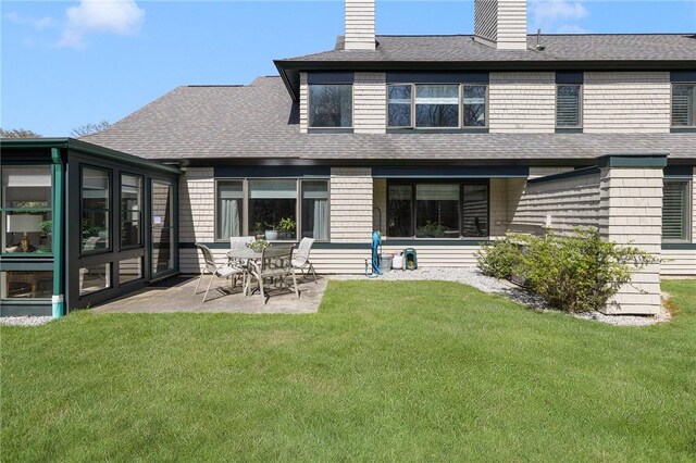 rear view of house featuring a lawn, a patio, a chimney, and a shingled roof