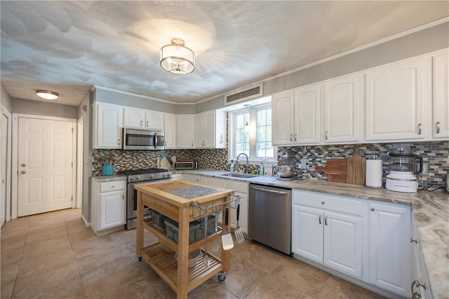 545 Central St, Burrillville, RI 02839 - kitchen featuring appliances with stainless steel finishes, a sink, backsplash, white cabinetry, and ornamental molding