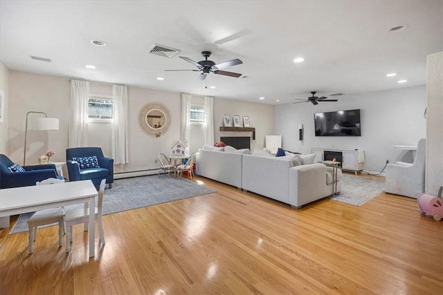 living area with light wood-type flooring, a ceiling fan, a warm lit fireplace, and visible vents
