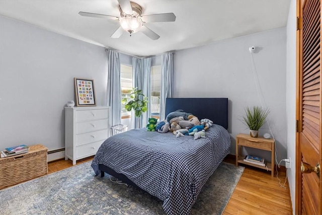 bedroom featuring ceiling fan, a baseboard heating unit, and wood finished floors