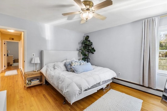 bedroom with a baseboard radiator, light wood finished floors, and ceiling fan