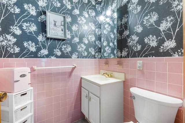 half bath featuring toilet, tile walls, wainscoting, and vanity