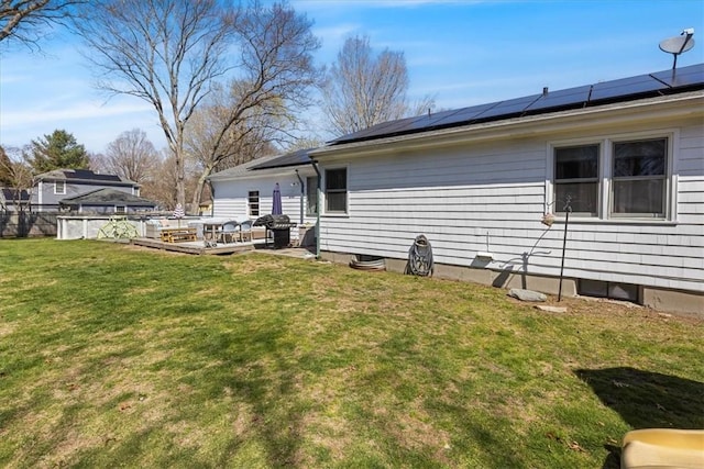 back of property featuring roof mounted solar panels, fence, a yard, and a deck
