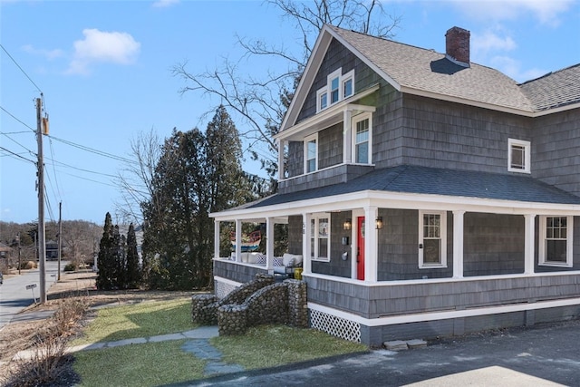 farmhouse inspired home with covered porch, a shingled roof, and a chimney