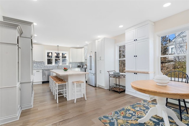 kitchen with a kitchen island, stainless steel dishwasher, high end refrigerator, light countertops, and light wood-style floors