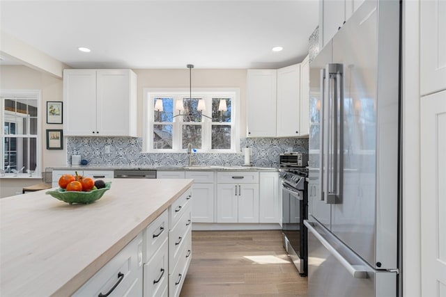 kitchen featuring light wood finished floors, light countertops, stainless steel appliances, white cabinetry, and backsplash