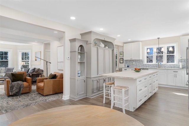 kitchen featuring decorative backsplash, open shelves, a sink, light wood-style floors, and a breakfast bar