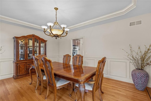 dining space with a decorative wall, ornamental molding, a notable chandelier, and visible vents