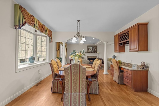 dining space featuring visible vents, baseboards, a lit fireplace, ornate columns, and light wood finished floors