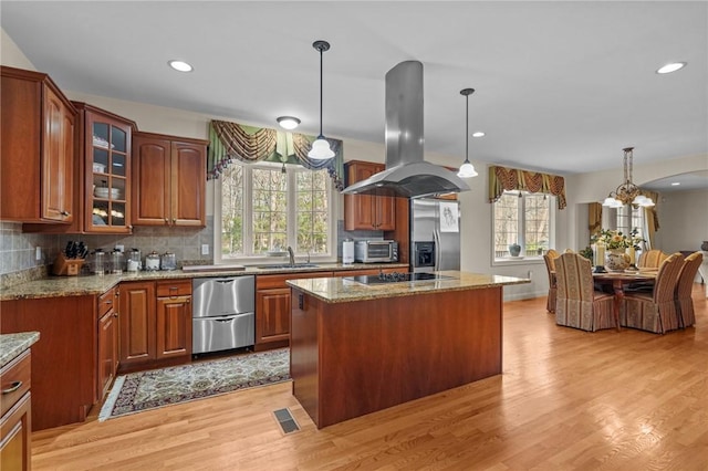 kitchen featuring appliances with stainless steel finishes, a sink, light wood-style floors, island range hood, and glass insert cabinets