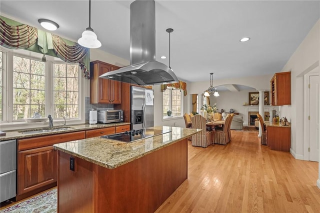 kitchen with brown cabinets, stainless steel fridge, a sink, a center island, and island range hood