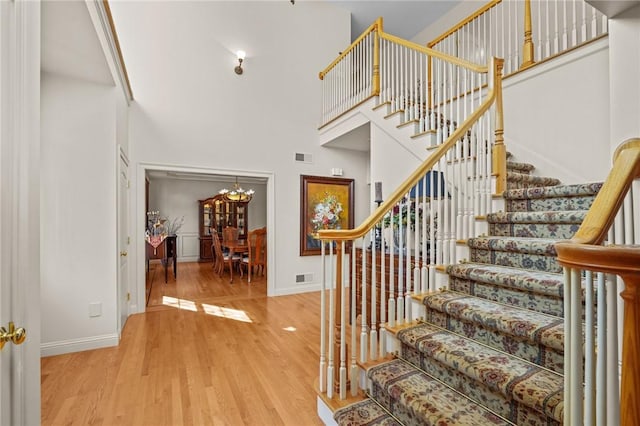 stairs with a high ceiling, an inviting chandelier, baseboards, and wood finished floors