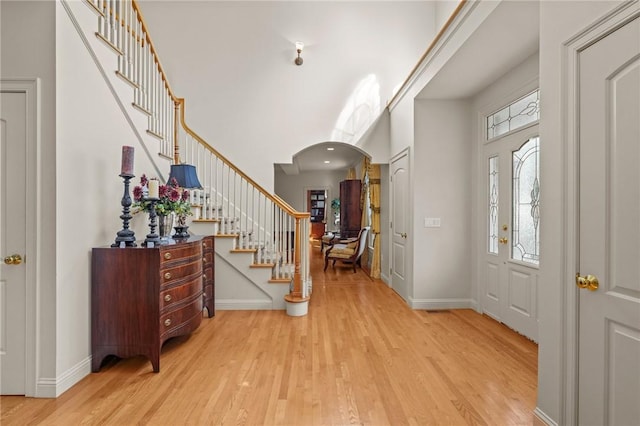 entrance foyer featuring baseboards, arched walkways, stairs, and wood finished floors
